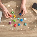 Top view of astrologer holding stones with zodiac sign beside laptop, coffee and constellations