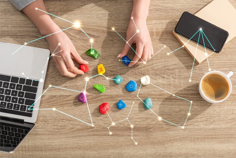 Top view of astrologer holding stones with zodiac sign beside laptop, coffee and constellations